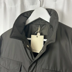 Olivgrön jacka från Rose & Born - Snygg olivgrön jacka från Rose & Born med en stilren design. Jackan har långa ärmar och två bröstfickor. Perfekt för en stilren look.