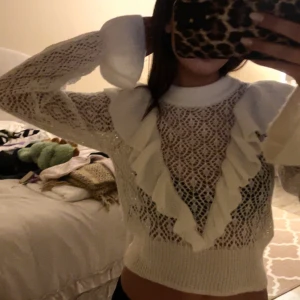 Vit spetsstickad tröja från Divided - Säljer en vit spetsstickad tröja från Divided med volangdetaljer framtill. Tröjan har långa ärmar och en ribbad nederkant. Perfekt för en stilren look med en twist. 🕊️