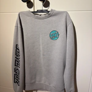 Santa Cruz sweatshirt  - Säljer en grå sweatshirt från Santa Cruz i storleken S. Tröjan har nån fläck på baksidan som kanske går att tvätta bort men bortsett från den fläcken så är tröjan i bra skick och har inga andra fläckar eller liknande.
