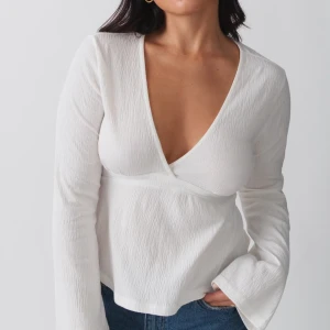 Vit topp med knytband - Säljer en stilren vit topp med långa ärmar och knytband i midjan. Toppen har en djup v-ringning och är tillverkad i ett lätt och bekvämt material. Skriv för egna bilder