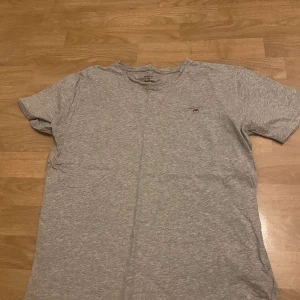 Grå t-shirt från GANT - Säljer en stilren grå t-shirt från GANT med ett litet tryck av deras logotyp på bröstet. T-shirten är kortärmad och tillverkad i mjukt bomullsmaterial. Sparsamt använd, priset går att diskutera! 