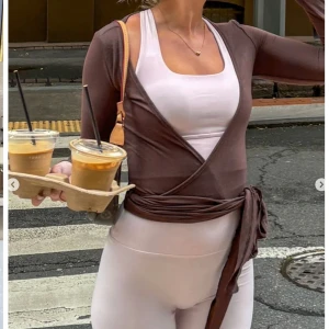 Brun omlottopp - Snygg brun omlottopp med långa ärmar och knytning i midjan från exercere . Perfekt för en stilren och bekväm look. Passar bra över ett linne eller topp. Använd en gång ny pris 758kr.