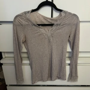 Beige långärmad topp från Intimissimi - Säljer en elegant beige långärmad topp från Intimissimi. Toppen har vackra spetsdetaljer vid halsringningen och ärmsluten, vilket ger den en romantisk touch. Perfekt för att lägga till en feminin känsla till din outfit.