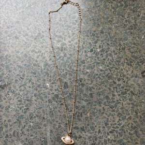 Guldhalsband med planetberlock - Guldhalsband med en unik planetberlock. Berlocken har en pärla i mitten som ger en extra touch av stil. Kedjan är tunn och justerbar med små dekorativa detaljer längs med. Perfekt för att lägga till en subtil men iögonfallande detalj till din outfit.