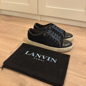 Blå sneakers från Lanvin - Snygga blå sneakers från Lanvin i mocka med snörning och en glansig tå. Skorna har en vit sula och kommer med en svart förvaringspåse med Lanvin-logga. Perfekta för en stilren look. 