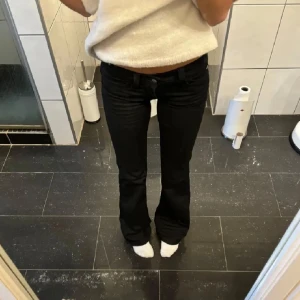 Svarta bootcut jeans - Snygga svarta bootcut jeans med låg midja. Perfekta för en stilren look. De har en klassisk design med knappar och dragkedja framtill. Storlek 25/30 passar mig som är 164