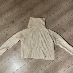 Vit stickad polotröja från Chiquelle - Säljer en mysig äggvit stickad polotröja från Chiquelle. Tröjan har en hög polokrage och långa ärmar, perfekt för kyliga dagar. Den är i en neutral färg som passar till det mesta. Perfekt att ha nu