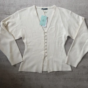 Fringe knited sweeter  - Säljer en stilren vit kofta från Gina Tricot i storlek S. Koftan har en v-ringad design med knappar framtill och är tillverkad av 50% Lenzing EcoVero viskos. Perfekt för en elegant och bekväm look. Slutsåld både på nätet och i butik många som vill ha den.