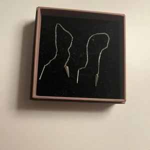 Häng örhängen med silver nitar - Eleganta silverörhängen med en tunn kedja och spetsiga hängen. Perfekta för att ge en stilren touch till din outfit. Från Edblad