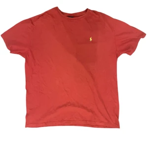 Röd t-shirt från Ralph Lauren - Säljer en klassisk röd t-shirt från Ralph Lauren med det ikoniska lilla broderade logotypen på bröstet. T-shirten är tillverkad i mjuk bomull och har en normal passform med korta ärmar. Perfekt för en avslappnad stil.                                                         📬| Skickas inom 24 timmar