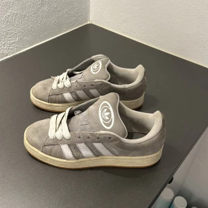 Grå Campus sneakers från Adidas  - Snygga grå sneakers från Adidas i mocka med vita detaljer och snörning. Perfekta för en avslappnad stil. Pris kan diskuteras 