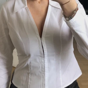 Vit figursydd skjorta med korsettdetalj - Snygg figursydd skjorta med korsettdetaljit med långa ärmar och knappar framtill. Perfekt för en stilren look. Säljer pga att den är för liten