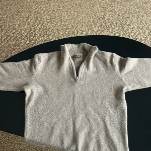 Beige stickad tröja från Stenströms - Säljer en stilren beige stickad tröja från Stenströms med dragkedja vid halsen. Perfekt för kyligare dagar med sin mjuka och bekväma passform. Tröjan har långa ärmar och en ribbad krage som ger en klassisk look.