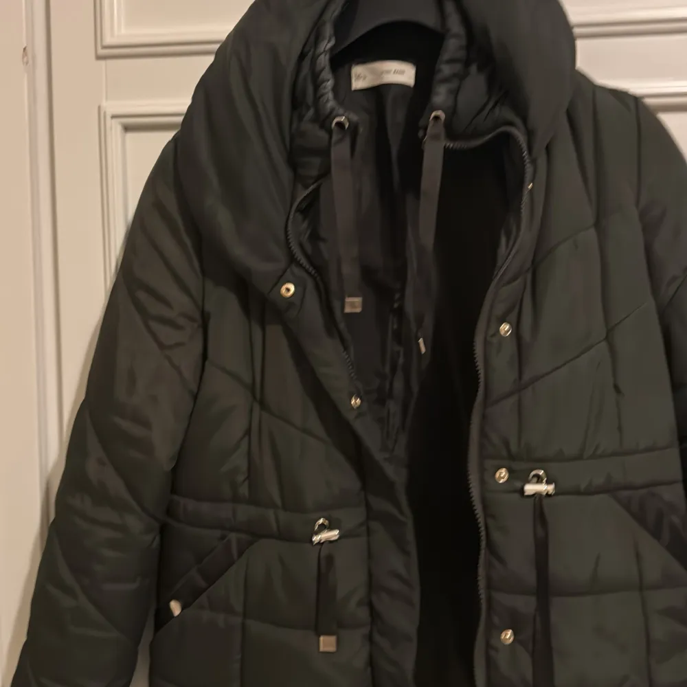 Snygg svart dunjacka från Sfera Basic med dragkedja och praktiska fickor. Jackan har en quiltad design och är perfekt för kyligare dagar. Den har långa ärmar och en bekväm passform.g. Takit.