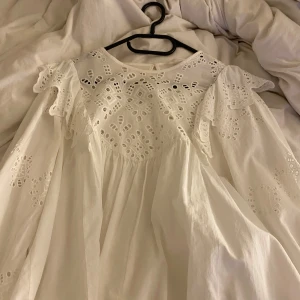 Vit blus med spetsdetaljer - Säljer en söt vit blus med vackra spetsdetaljer och volanger. Blusen har långa ärmar och en luftig passform, perfekt för vår och sommar. Den har en gullig känsla med sina fina broderier och är lätt att matcha med olika outfits.💗💗