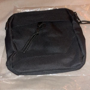 Svart axelväska med dragkedja - Snygg och praktisk svart axelväska i syntetmaterial. Väskan har en dragkedja framtill för enkel åtkomst till dina saker. Perfekt för att bära med sig det nödvändigaste på språng.