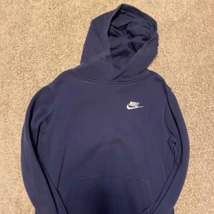 Mörkblå Nike hoodie - Säljer min mörkblåa Nike hoodie eftersom den är för liten och kommer inte till användning. Skicket är 9/10 och ser ut som ny för jag har bara använt den ett fåtal gånger. Den e storlek L i barnstorlek 