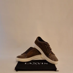 Bruna sneakers från Lanvin - Säljer ett par snygga bruna sneakers från Lanvin i bra skick. De har en stilren design med snörning och en vit sula som ger en fräsch kontrast. Perfekta för både vardag och fest! Kommer med originalpåse!