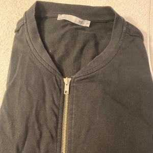 Svart tröja med dragkedja - Säljer en svart tröja med dragkedja framtill. Den har en enkel och stilren design med långa ärmar. Perfekt för både vardag och lite kyligare kvällar. Passar bra till jeans eller kjol!