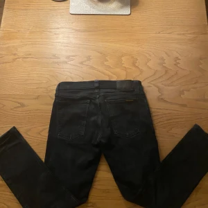 Svarta jeans från Nudie Jeans - Säljer ett par svarta jeans från Nudie Jeans i mycket bra skick. De har en klassisk femficksdesign och är tillverkade i ett slitstarkt denimtyg. Perfekta för både vardag och fest! Det säger w29 men det passar bättre för w28