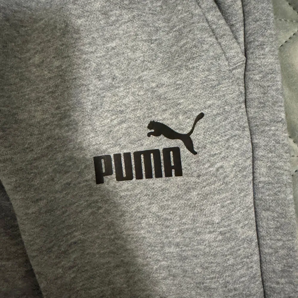 Säljer ett par grå mjukisbyxor från Puma i mycket bra skick. De är superbekväma med elastisk midja och snörning för perfekt passform. Byxorna har ribbade muddar vid bensluten och en klassisk Puma-logga på benet. Perfekta för chill eller träning!. Jeans & Byxor.