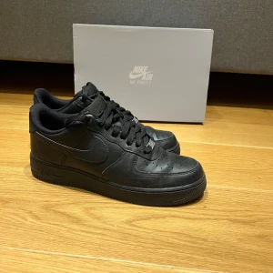 Svarta Nike Air Force 1 - Säljer ett par klassiska svarta Nike Air Force 1 i skinn. De är i nytt skick och har en stilren design med snörning. Kommer med originalkartong. Storlek 44, man storlek