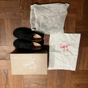 Svarta sneakers med nitar från Christian Louboutin - Säljer ett par svarta sneakers i mocka från Christian Louboutin. Skorna har coola nitar på tån och den ikoniska röda sulan. De är i mycket bra skick och kommer med originalkartong och dustbags. Perfekta för att ge din outfit en edgy touch! Kort medföljer. Pris är ej hugget i sten.