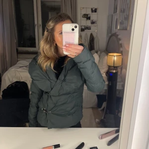Mörkgrön pufferjacka - Säljer en snygg mörkgrön pufferjacka i mycket bra skick. Jackan har en cool omlott-design med knappar och är perfekt för höst och vinter. Den är långärmad och har en normal passform. Perfekt för att hålla sig varm och stilren under kyliga dagar! Går att knäppa uppe vid halsen på olika sätt beroende på hur öppen man vill ha den, två alternativ finns på bilderna ❤️storlek 38 men passar mig som har xs!