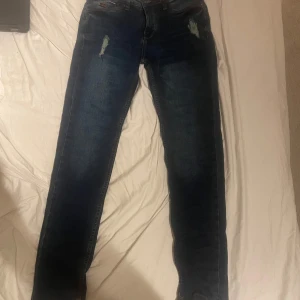 Mörkblå jeans från Sublevel - Säljer ett par mörkblå jeans från Sublevel i nytt skick. De har en snygg slitning på låren och en klassisk femficksdesign. Perfekta för en casual look eller en utekväll. Passar bra till både sneakers och boots!