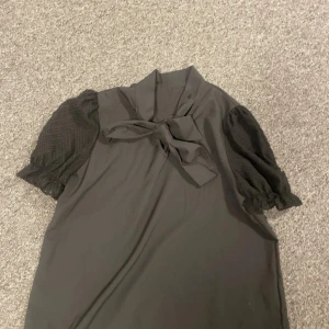 Svart blus med knyt och spetsdetaljer - Säljer min svarta blus med knyte vid halsen. Aldrig använd och är i nytt skick.