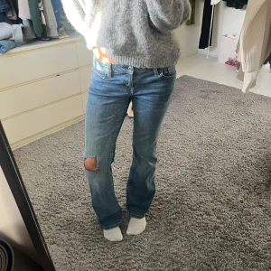 Blå lågmidjade bootcut jeans med hål - Säljer ett par snygga blå lågmidjade jeans med slitningar på knäet. Jag har klippt hålet själv. Bra skick!!☺️☺️