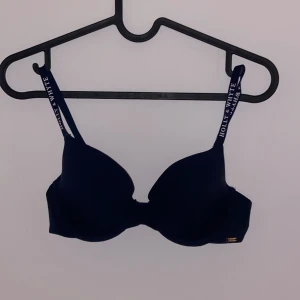 Svart BH från Holly & White - Snygg svart BH från Holly & White med justerbara axelband. Perfekt för vardagsbruk med en stilren design. Axelbanden har märkesloggan tryckt i vitt för en extra touch.