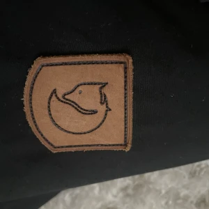 Svart jacka från Fjällräven - Säljer en svart jacka från Fjällräven i mycket bra skick. Den har en stilren design med dragkedja och knappar framtill.  Fjällrävens logga syns på ärmen. Passar både till vardags och utomhusaktiviteter. 