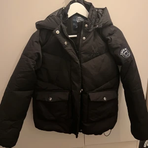 Svart svea jacka - Svart svea jacka me luva i storlek 170 perfekt till vintern. Jackan har 4 framfickor som finns synliga på första bilden. Fickorna är de med knappar samt så finns det två ”gömda” på ytterkanten. Det finns även en liten ficka med kardborreband på insidan. I övrigt finns det inget att anmärka på jackan dvs att jackan är hel. Exra knappar tillkommer. Ursprungligt pris 1 399kr