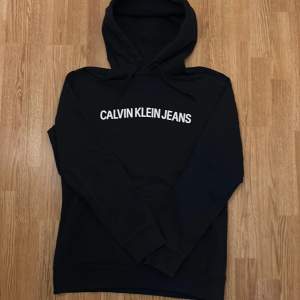 Säljer en stilren svart hoodie från Calvin Klein Jeans i storlek L. Den har en klassisk design med vit logga på bröstet och är perfekt för både vardag och chill. Superbekväm och passar till allt!  Den är använd en gång och är i helt nytt skick.