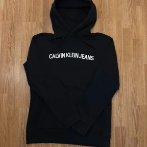 Svart hoodie från Calvin Klein Jeans. Helt nytt skick som är använd 1 gång. - Säljer en stilren svart hoodie från Calvin Klein Jeans i storlek L. Den har en klassisk design med vit logga på bröstet och är perfekt för både vardag och chill. Superbekväm och passar till allt!  Den är använd en gång och är i helt nytt skick.