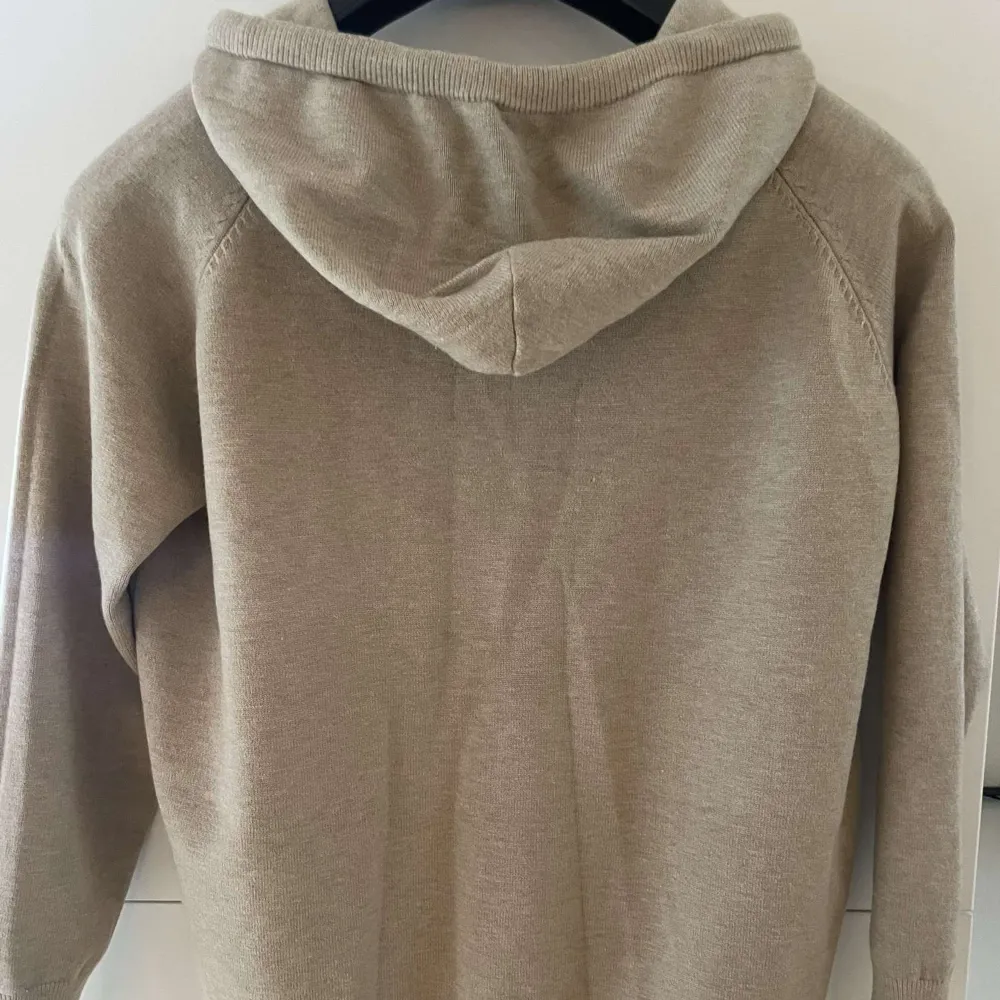 Säljer en stilren beige hoodie i mjukt bomullsmaterial. Perfekt för höst och vår med sin bekväma passform och långa ärmar. Den har en klassisk huva med dragsko och ribbade muddar vid ärmslut och nederkant. Enkelt att matcha med det mesta i garderoben!. Tröjor & Koftor.