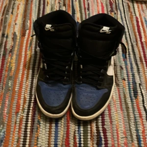 Nike Air Jordans i svart, blå och vit - Säljer ett par Nike Air Jordans i svart, blå och vit. Skorna har klassisk snörning och är i bra skick. Perfekta för både vardag och fest! Storleken är herr 44. Passa på att köpa dessa ikoniska sneakers! Pris kan diskuteras vid snabb affär! Samt defekt där bak.