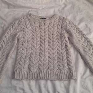 Beige stickad tröja från H&M - Mysig beige stickad tröja från H&M i storlek S. Den har ett klassiskt flätmönster och är perfekt för kyliga dagar. Tröjan är långärmad och har ribbade muddar vid ärmslut och nederkant. Perfekt för höst och vinter! Använd knappast