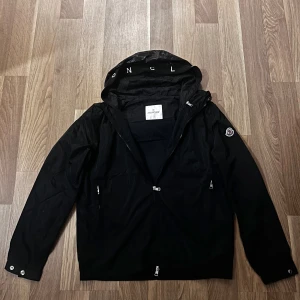 Svart jacka från Moncler - Säljer en snygg svart jacka från Moncler i mycket bra skick. Jackan har en dragkedja framtill och en huva med Moncler-logga. Perfekt för höst och vinter, med en stilren design som passar till det mesta.