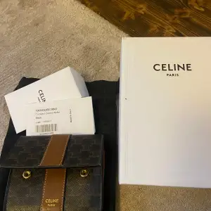 Säljer en elegant Celine plånbok i svart och brunt med guldiga detaljer. Plånboken har ett klassiskt mönster och är tillverkad i skinn. Perfekt för att hålla ordning på kort och kontanter med stil. Kommer med originalförpackning. Väldigt fin på utsidan men märken på insidan som bild visar. Kommer med låda påse och tag.