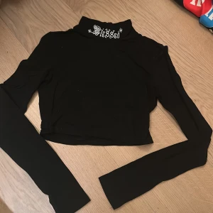 Svart croppad polotröja - Säljer en svart croppad polotröja med texten 'Blessed' broderad i vitt på kragen. Tröjan har långa ärmar och är perfekt för en cool och avslappnad stil 💗