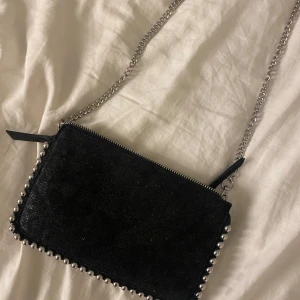 Svart väska - Snygg svart axelväska med silverkedja och dragkedja. Väskan har coola nitar längs kanterna som ger en edgy look. Perfekt för både vardag och fest! 🖤