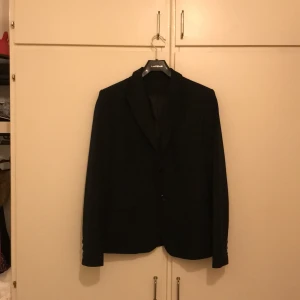 Svart kavaj - Snygg svart kavaj från Lardini i klassisk stil. Perfekt för både formella och semi-formella tillfällen. Kavajen har en elegant passform med två knappar framtill och är tillverkad i ett material som ger en lyxig känsla. Ett måste i garderoben för den stilmedvetne!