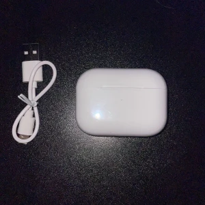 Trådlösa hörlurar med laddningsetui   - Säljer ett par vita trådlösa hörlurar med laddningsetui. Hörlurarna har en stilren design och kommer med en USB-laddningskabel. Perfekt för musik och samtal på språng.