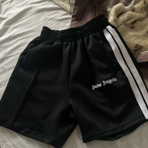 Svarta shorts från Palm Angels - Snygga svarta shorts från Palm Angels med vit sidoremsa och elastisk midja. Perfekta för en avslappnad stil. Priset kan diskuteras 