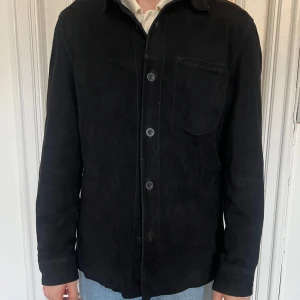 Svart Mockajacka Jofama - Snygg svart mockajacka/overshirt med knappar framtill och en bröstficka. Perfekt för lager-på-lager-stil och passar till många olika outfits. Enkelt och stilrent plagg för alla tillfällen. Storlek 52, passar även 50. Se mina övriga annonser för fler grymma plagg! 