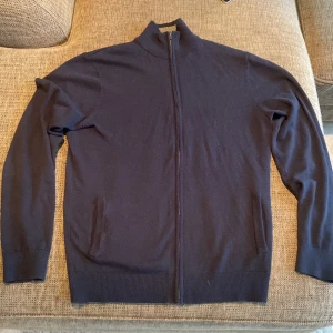 Mörkblå full zip - Säljer en stilren mörkblå full zip. Perfekt för kyligare dagar och enkel att matcha med olika outfits. Koftan har långa ärmar och ribbade muddar vid ärmslut och nederkant. Storlek L men passar mer M. Helt ny med lappar kvar.