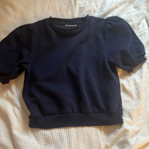 Mörkblå tröja från Gina Tricot - Säljer en stilren mörkblå tröja från Gina Tricot. Tröjan har korta puffärmar och en rund halsringning med ribbade kanter. Perfekt för en avslappnad look.