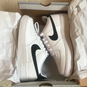 Vita Nike Air Force med svart swoosh - Säljer ett par sprillans nya klassiska vita Nike Air Force med svart swoosh. Skorna har snörning och är i syntetmaterial. Perfekta för en stilren look. Storlek 38,5